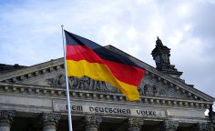 Deutschlandfahne vor dem Deutschen Bundestag Deutsche Flagge weht vor dem Reichstagsgebäude in Berlin, Fassade mit Schriftzug „Dem Deutschen Volke“.