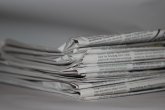 Stapel gefalteter Zeitungen in Nahaufnahme, grauweißes Papier mit sichtbarem Text, unscharfer Hintergrund.