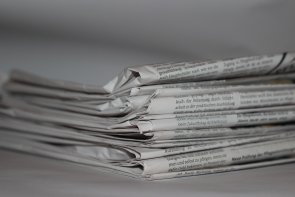 Stapel gefalteter Zeitungen in Nahaufnahme, grauweißes Papier mit sichtbarem Text, unscharfer Hintergrund.