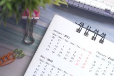 Kalender Aufgeschlagener Schreibtischkalender mit Spiralbindung, daneben Stifthalter, bunter Clip und Karotten-Büroklammer auf hellem Untergrund.